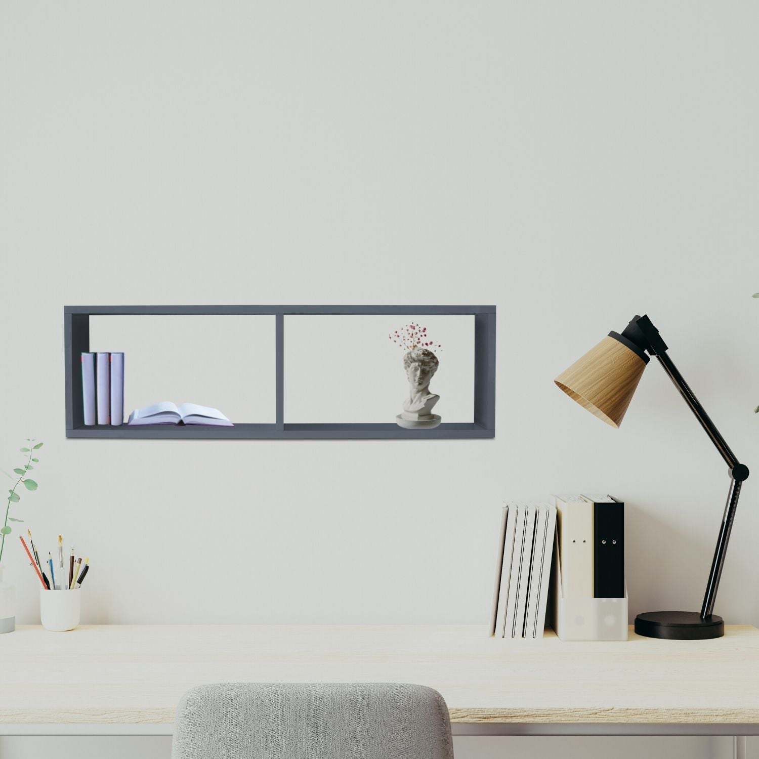 Wandregal COMPACT Anthrazit hängt über einem Büroschreibtisch. Auf dem Schreibtisch steht eine Tischlampe, Bücher, Stiftehalter mit Stiften. Eine Stuhllehne ist zu sehen.