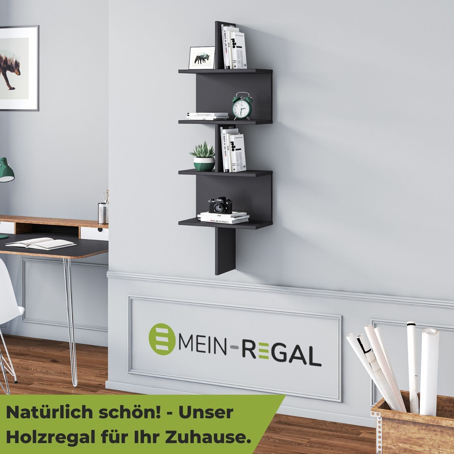 Wandregal Otto Schwarz im Büro neben einem Schreibtisch und Wandbild an grauer Wand hängend. Im Regal stehen Bücher, eine Kaktuspflanze, Fotoapparat, Wecker.