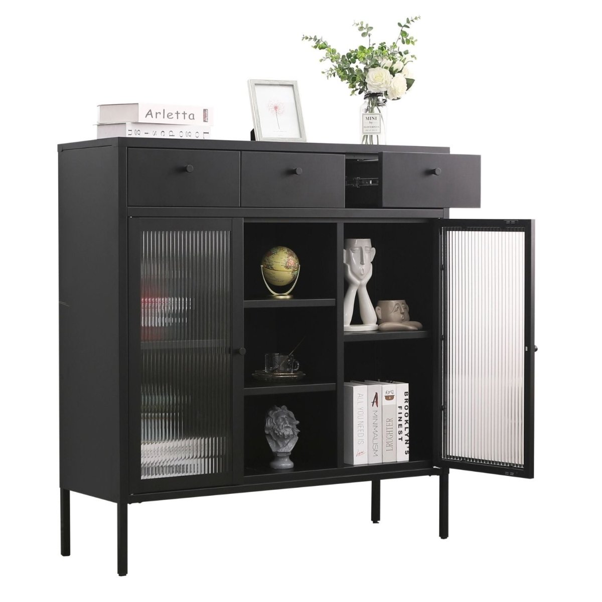 Kommode Paris Schwarz aus Metall mit 3 Schubladen, 3 Fächern, 2 Glastüren. Eine Glastür und eine Schublade ist geöffnet. Dekoartikel sind zu sehen. Oben drauf liegen Bücher, ein Bilderrahmen und eine Glasvase mit Blumen stehen. Der Hintergrund ist weiß.