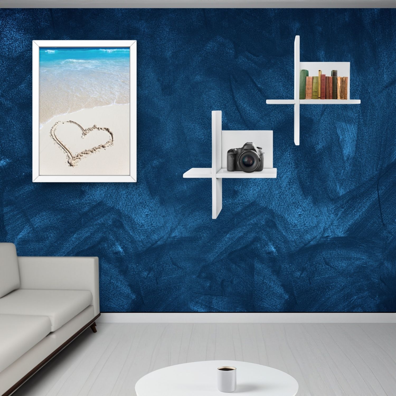 Wandregal Brick Weiß hängend an einer blauen Wand im Wohnzimmer. Links daneben hängt ein Wandbild. Links unten sieht man ein Stück helles Sofa. Ein Couchtisch mit Tasse Kaffee.
