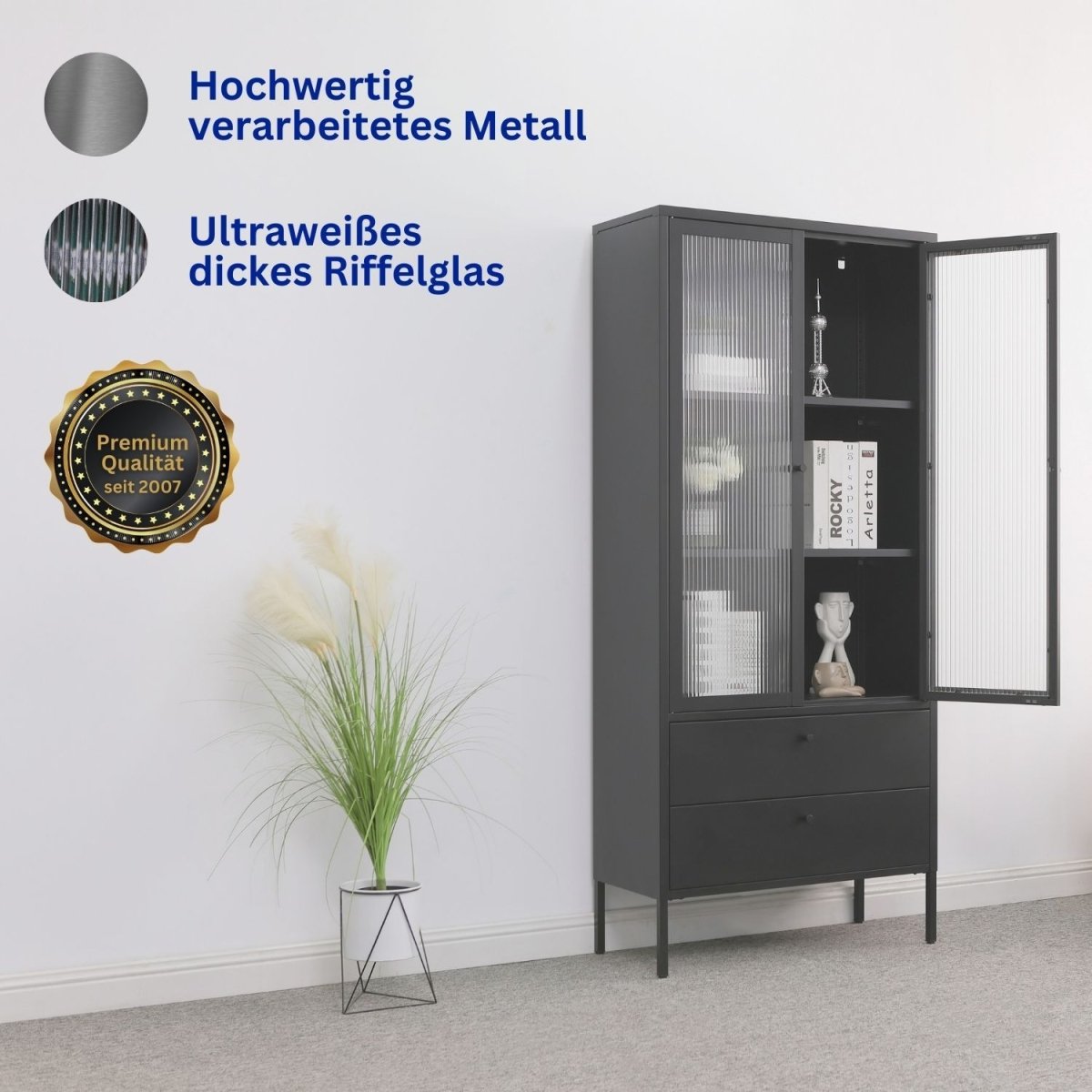Vitrine Paris Schwarz aus Metall in einem Zimmer. Eine Tür ist geöffnet und zeigt den Inhalt. Daneben steht eine Zimmerpflanze.